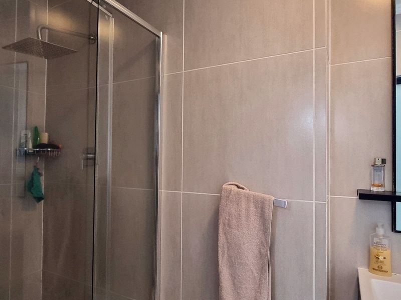 Modern bathroom featuring a glass-enclosed rain shower, neutral wall tiling, and a sleek vanity area with a wall-mounted mirror.
