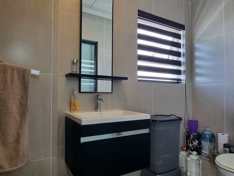 Modern bathroom featuring a wall-mounted vanity, ceramic basin, dual-flush toilet, and neutral wall tiling with a functional roller blind.
