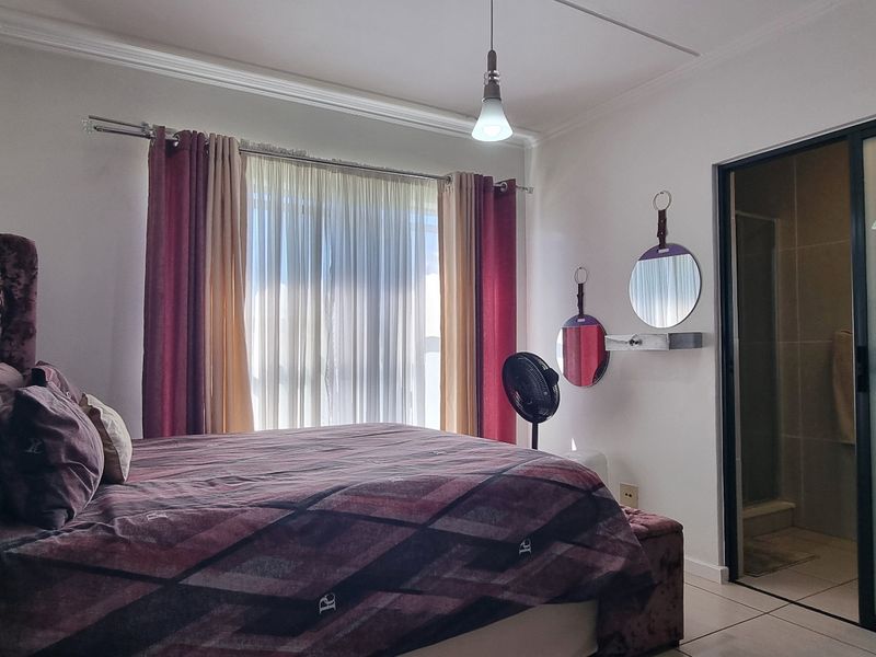 A well-lit bedroom featuring tiled flooring, crown molding, and direct access to an en-suite bathroom through a sliding glass door.