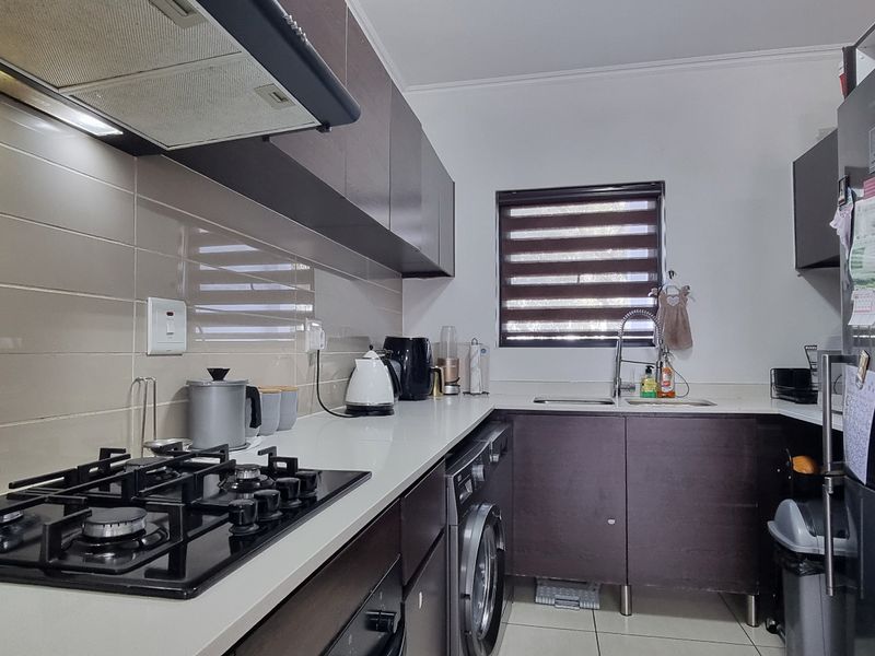 Modern kitchen featuring dark laminate cabinetry, stone countertops, gas hob with extractor fan, integrated washing machine, and tiled splashback.