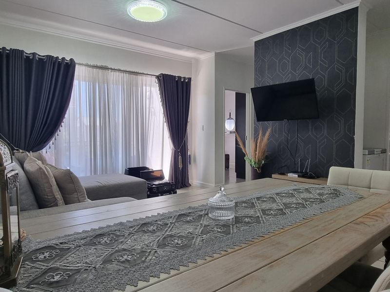 An open-plan living and dining area featuring tiled floors, a decorative feature wall, and large windows with curtain tracks.