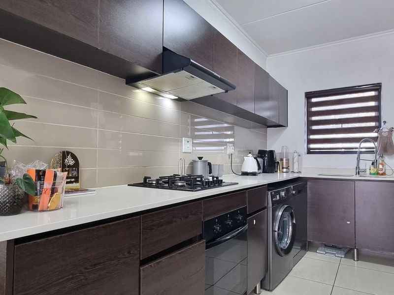 Modern kitchen featuring dark wood cabinetry, stone countertops, integrated gas hob, built-in oven, and tiled backsplash with neutral floor tiles.