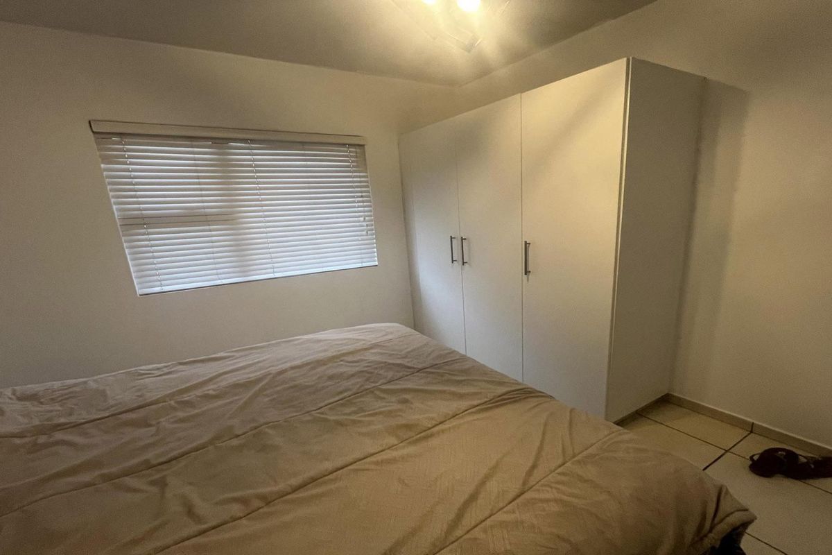 A bedroom featuring tiled flooring, a built-in wardrobe, and a window fitted with venetian blinds.
