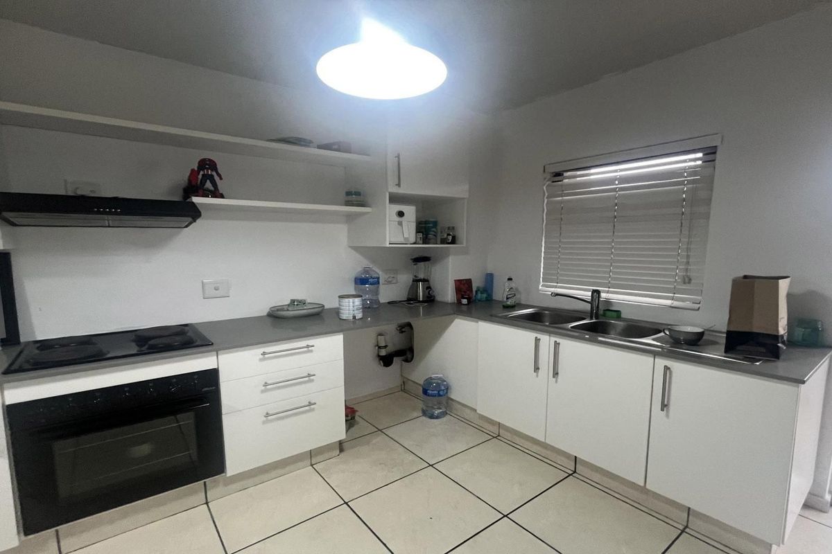 A functional kitchen featuring white cabinetry, a built-in oven with hob, double sink, and tiled flooring. Note the missing cabinet door under the sink.