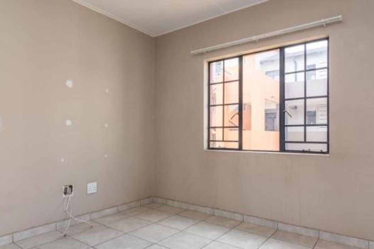 An empty bedroom featuring tiled flooring, a window with security bars, and neutral wall finishes requiring minor cosmetic attention.