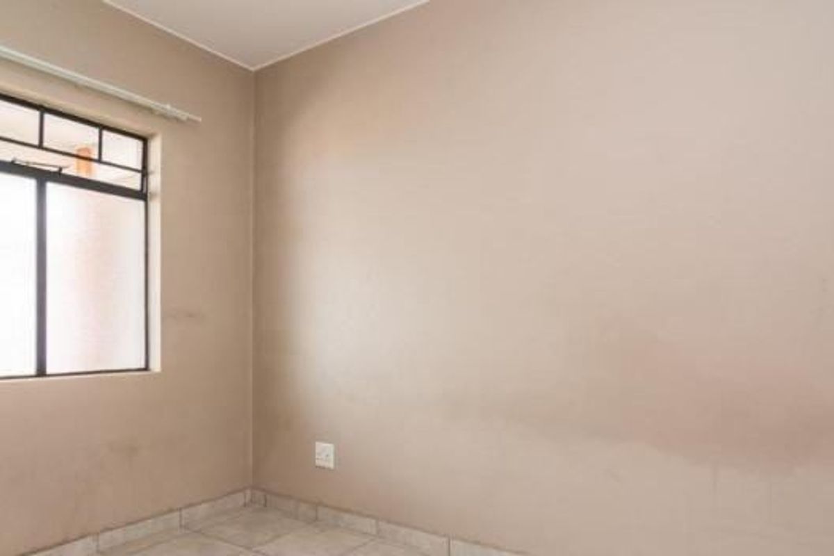 An empty bedroom featuring tiled flooring and a window with security bars, requiring minor cosmetic updates to the walls.