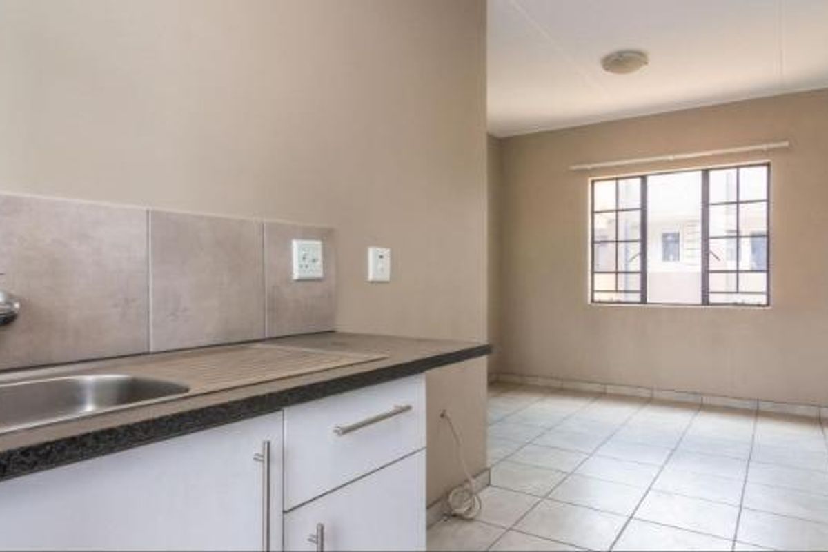 A clean, empty kitchen area featuring a stainless steel sink, tiled splashback, and neutral cabinetry, offering a functional space ready for customization.