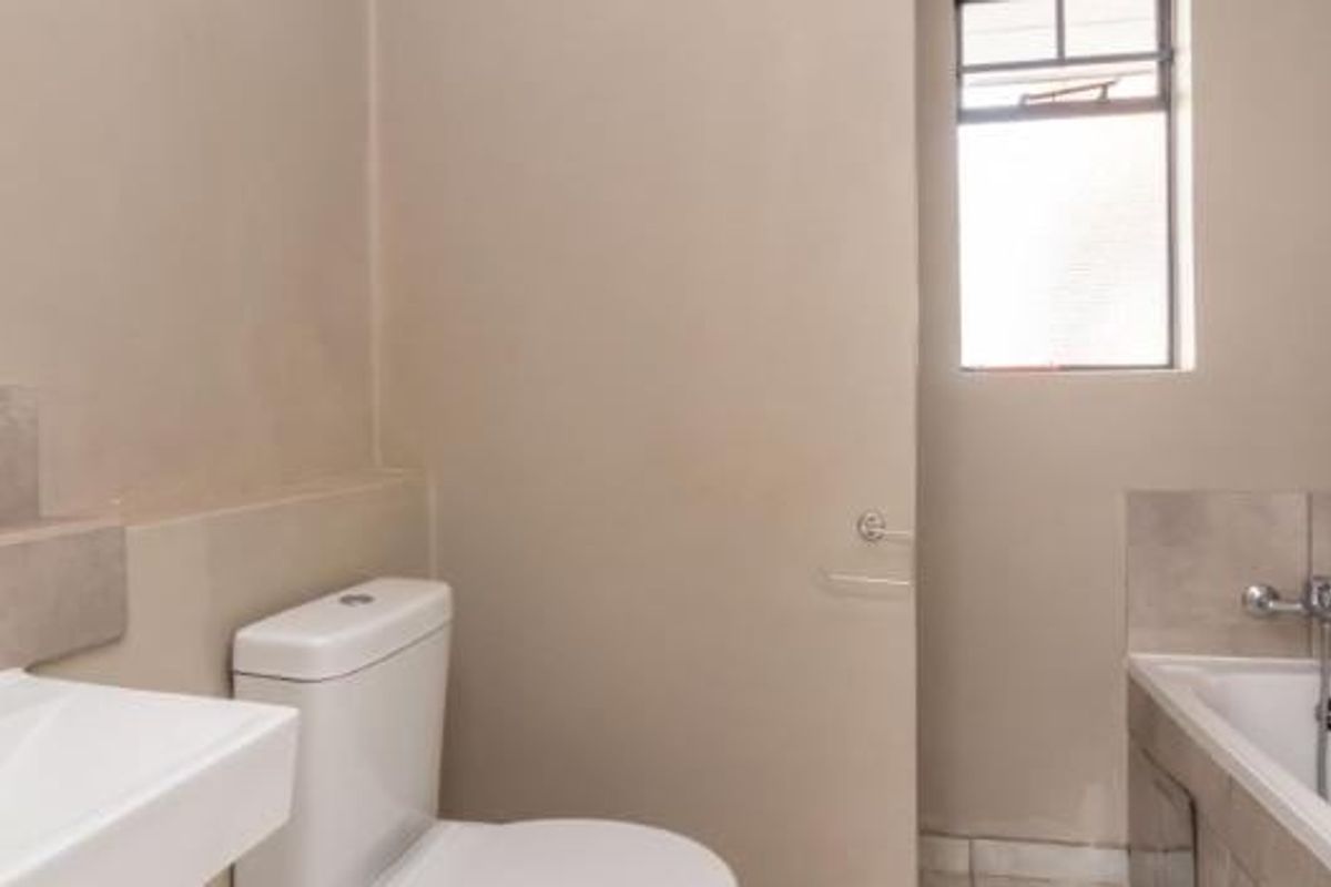 A functional bathroom featuring a basin, toilet, and bathtub with neutral wall finishes and natural light from a window.