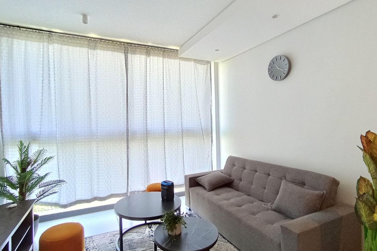 A bright living room featuring large floor-to-ceiling windows with curtains and recessed ceiling lighting, creating a clean and modern atmosphere.