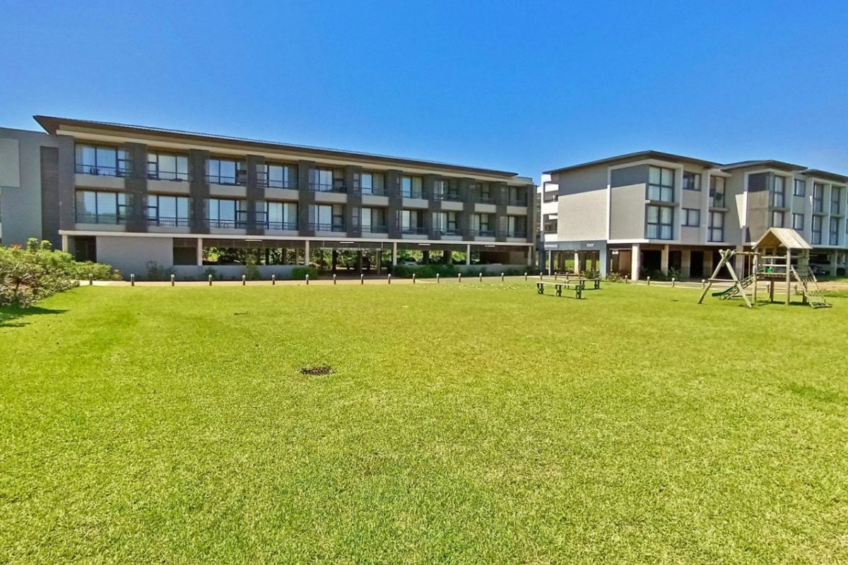 A view of the rear exterior of a multi-story apartment complex featuring modern architecture, private balconies, and a large, well-maintained communal lawn area.