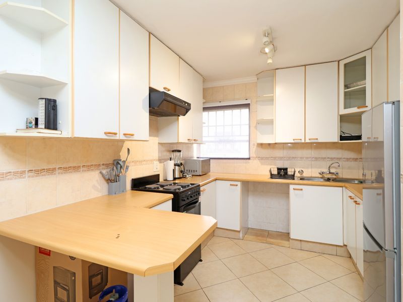A functional kitchen featuring white cabinetry, laminate countertops, tiled backsplash, and tiled flooring, offering a practical layout for daily meal preparation.