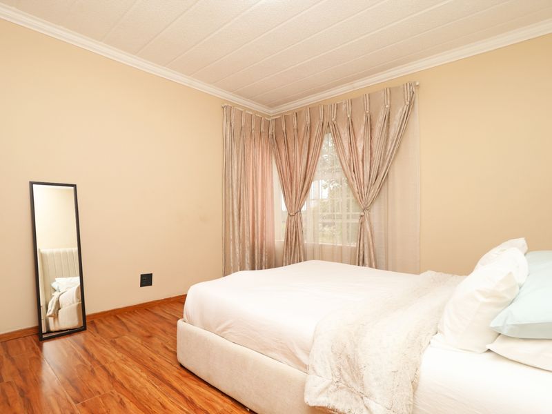 A bedroom featuring laminate flooring, textured ceiling with cornice detailing, and a corner window arrangement.