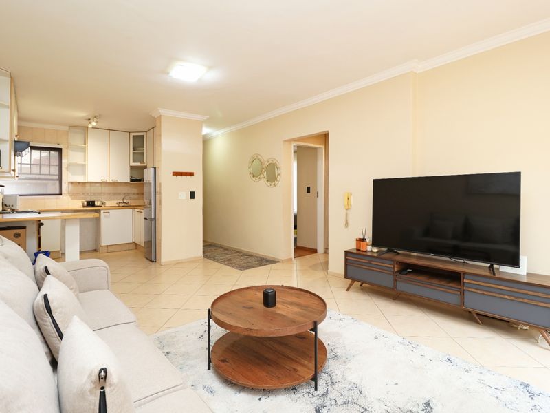 Open-plan living area featuring a functional kitchen with built-in cabinetry and tiled flooring, seamlessly connected to the main lounge space.