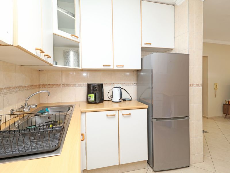 A functional kitchen featuring laminate countertops, tiled backsplash, and ample built-in cabinetry, leading into an adjacent living area.