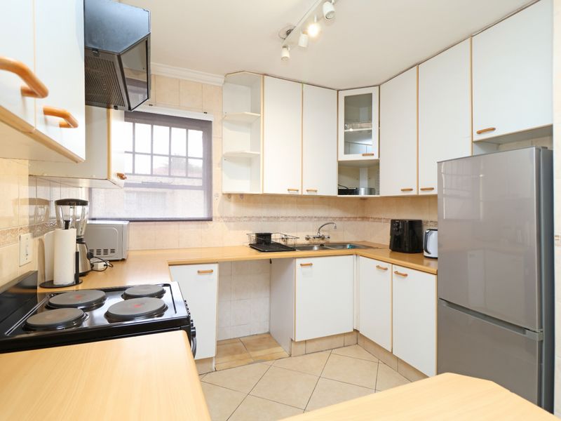 Functional kitchen featuring white cabinetry, laminate countertops, tiled backsplash, and integrated electric hob with extractor fan.