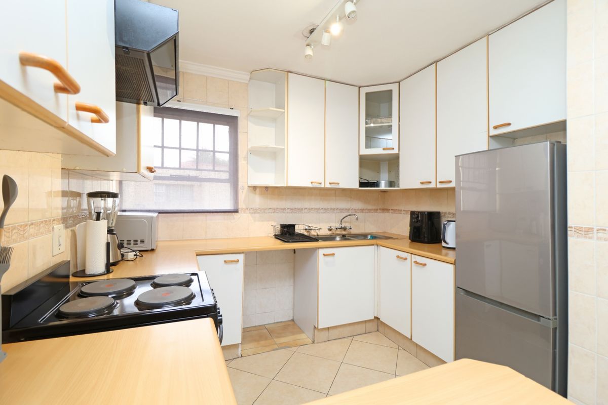 Functional kitchen featuring white cabinetry, laminate countertops, tiled backsplash, and integrated electric hob with extractor fan.