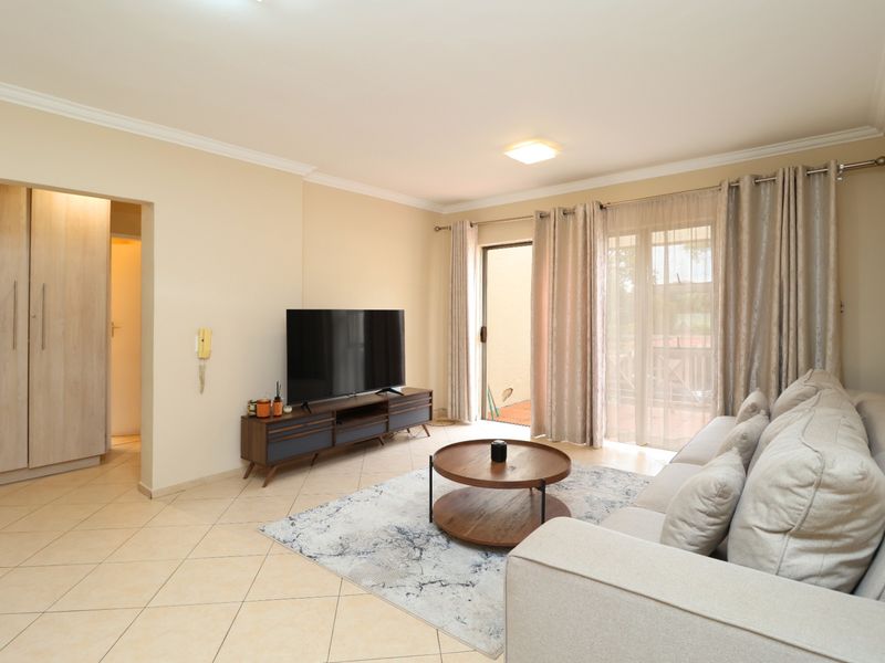 A bright and well-maintained living room featuring tiled flooring, neutral walls, and a sliding glass door providing access to the outdoor area.
