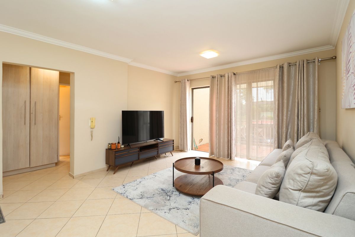A bright and well-maintained living room featuring tiled flooring, neutral walls, and a sliding glass door providing access to the outdoor area.