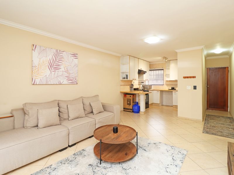 Open-plan living area featuring tiled floors, coved ceilings, and a functional kitchen with built-in cabinetry and an extractor fan.