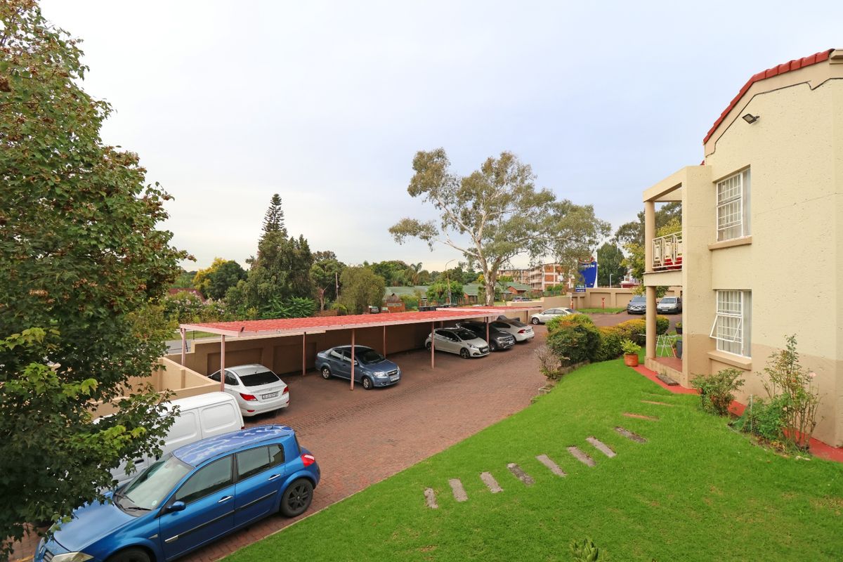 View of the townhouse complex exterior featuring a paved driveway, covered parking bays, and a well-maintained lawn area.