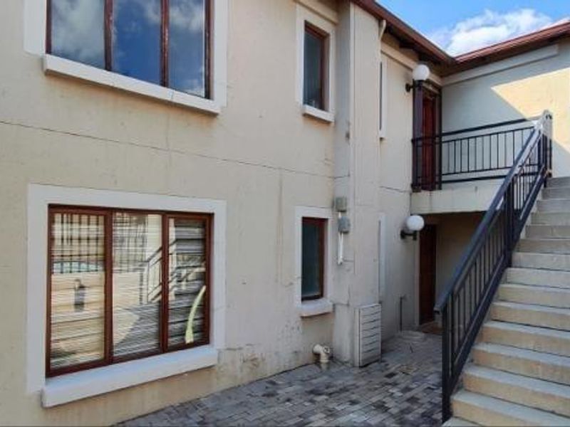 Exterior view of an apartment building featuring a paved courtyard, external staircase with metal railings, and timber-framed windows.