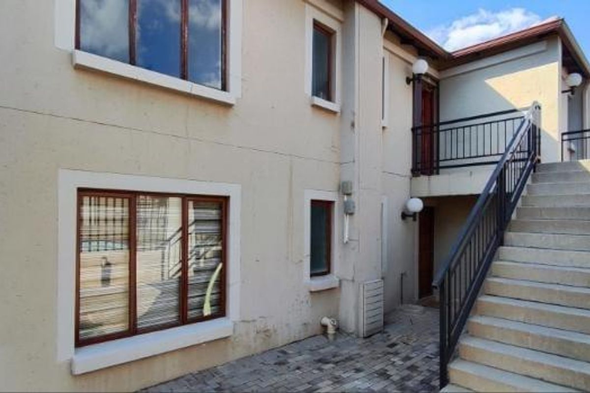 Exterior view of an apartment building featuring a paved courtyard, external staircase with metal railings, and timber-framed windows.