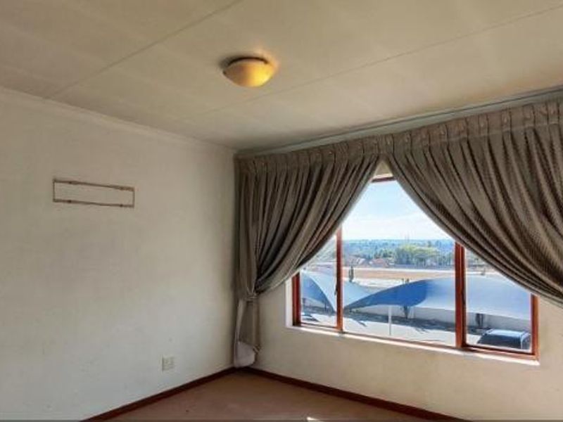 A bright, empty bedroom featuring large windows with curtains and a view, providing a blank canvas for personalization.