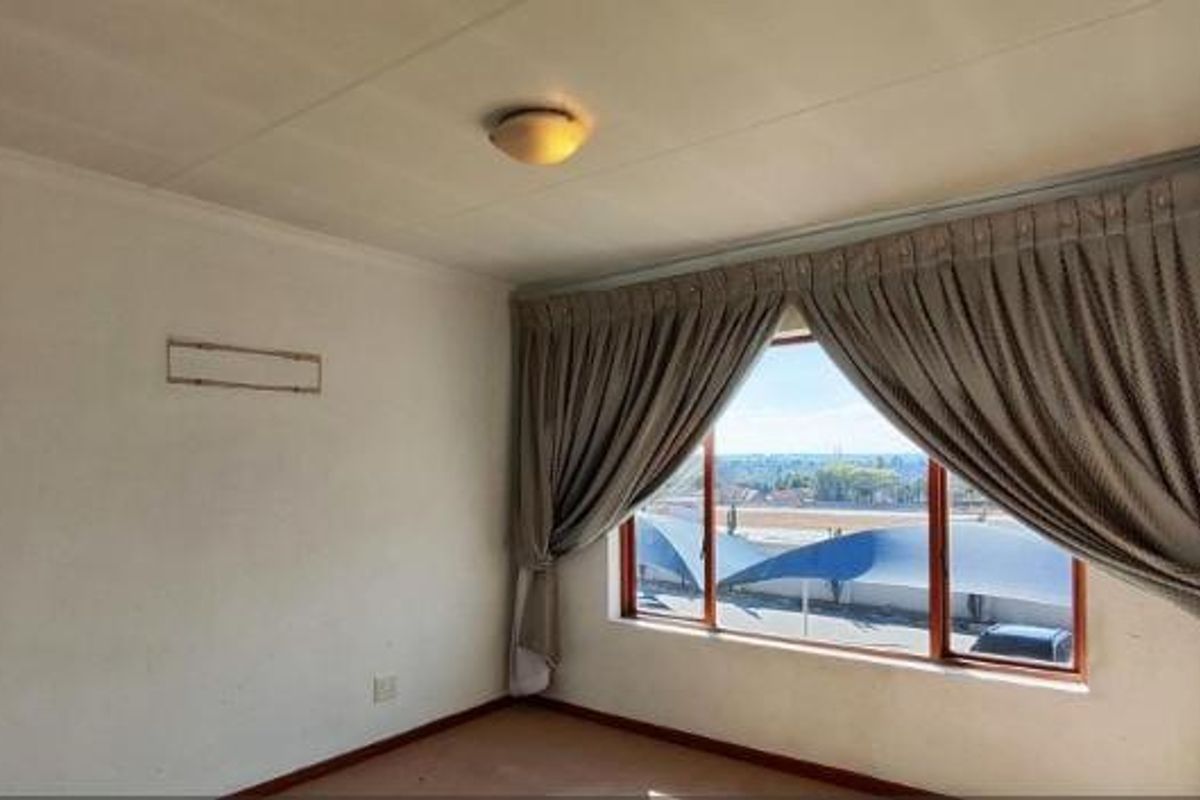A bright, empty bedroom featuring large windows with curtains and a view, providing a blank canvas for personalization.