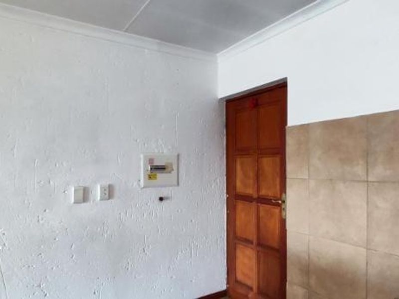 An interior view showing a textured wall with an electrical distribution board, a timber door, and a tiled wall section.