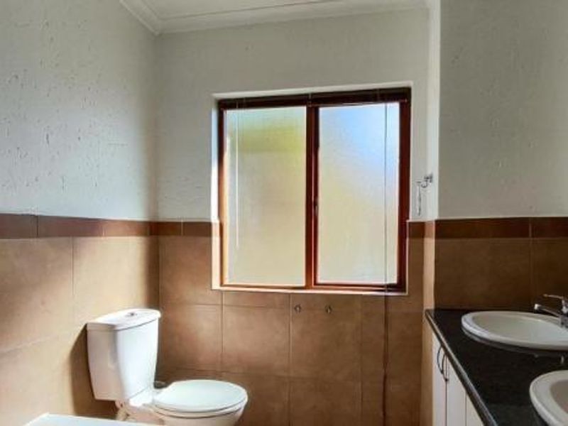 A dated bathroom featuring a dual vanity, ceramic wall tiling, and a toilet, requiring cosmetic updates to improve the overall aesthetic.