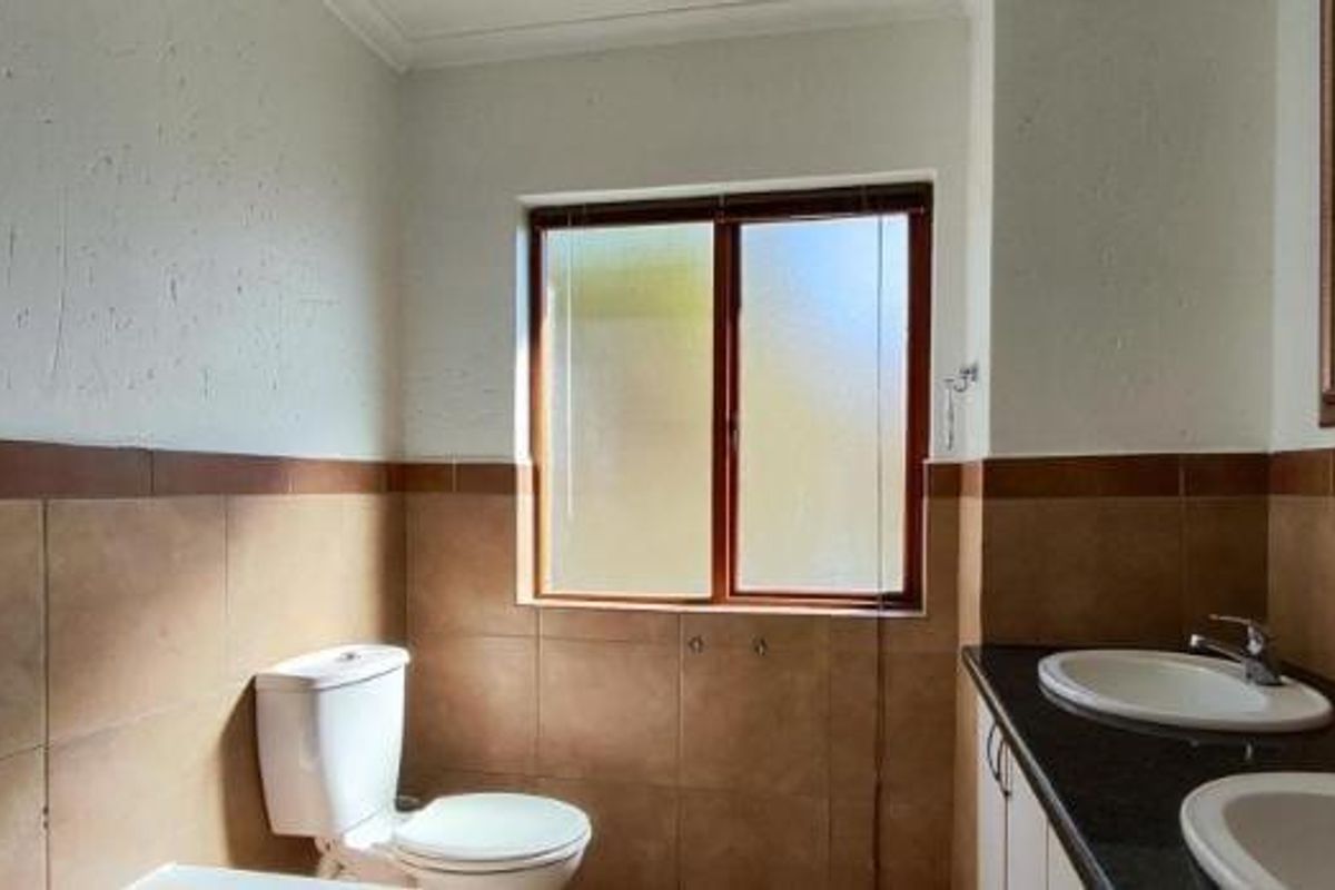A dated bathroom featuring a dual vanity, ceramic wall tiling, and a toilet, requiring cosmetic updates to improve the overall aesthetic.
