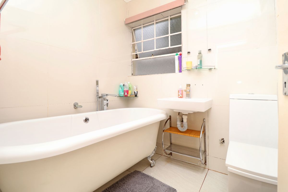 A functional bathroom featuring a classic clawfoot bathtub, wall-mounted basin, and toilet, finished with neutral wall and floor tiles.