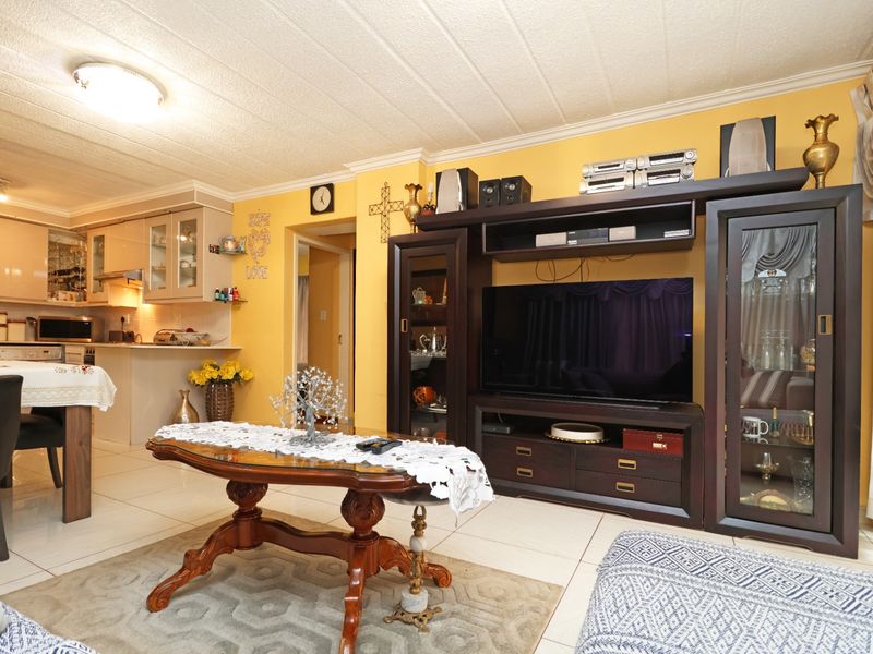 Open-plan living and kitchen area featuring tiled flooring, neutral yellow walls, and functional built-in cabinetry, offering a combined space for dining and relaxation.
