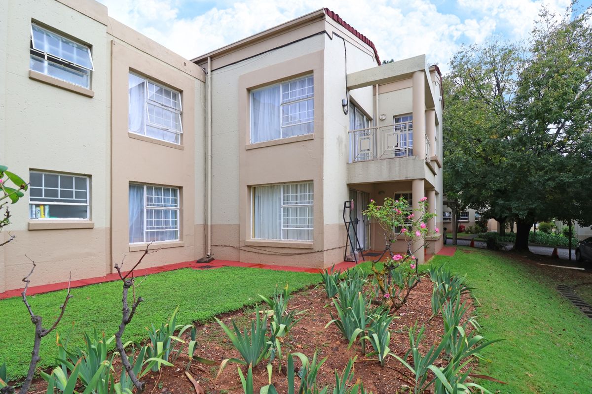 Rear view of the apartment building featuring a landscaped garden, balcony with metal balustrade, and multi-pane casement windows.