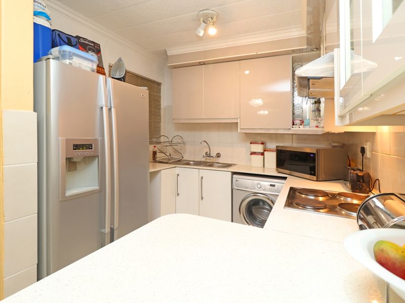 Compact kitchen featuring high-gloss cabinetry, laminate countertops, integrated washing machine, electric hob, and tiled backsplash.
