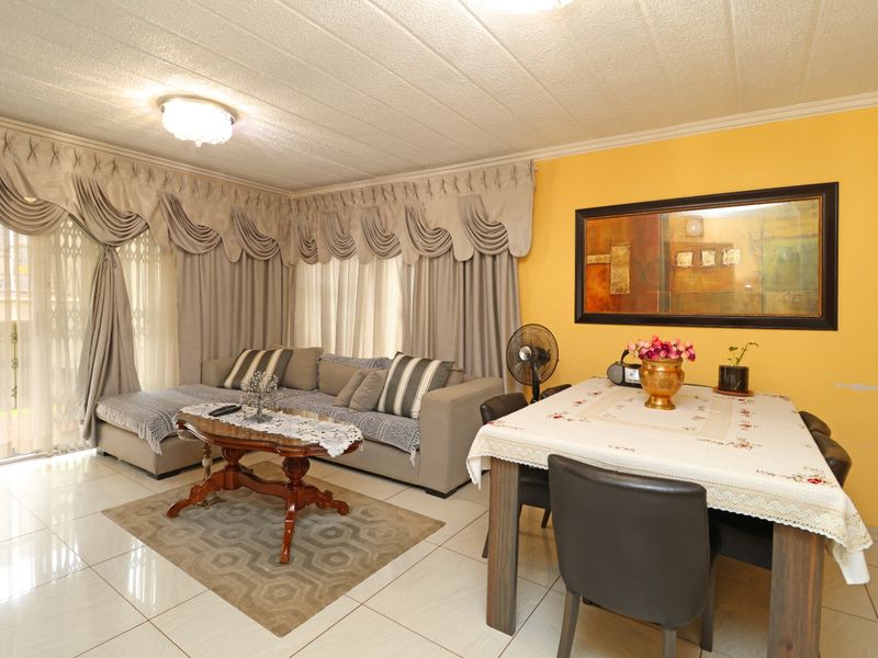 Open-plan living and dining area featuring tiled flooring, textured ceilings, and a sliding glass door with security gate access to the exterior.