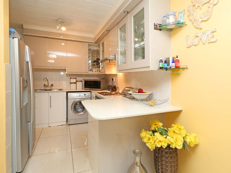 Compact kitchen featuring modern high-gloss cabinetry, stone countertops, integrated appliances, and tiled flooring, offering a functional and efficient workspace.
