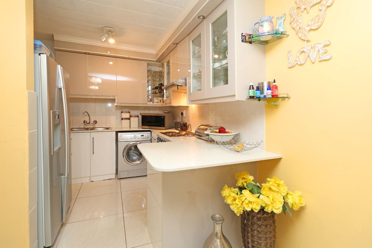 Compact kitchen featuring modern high-gloss cabinetry, stone countertops, integrated appliances, and tiled flooring, offering a functional and efficient workspace.