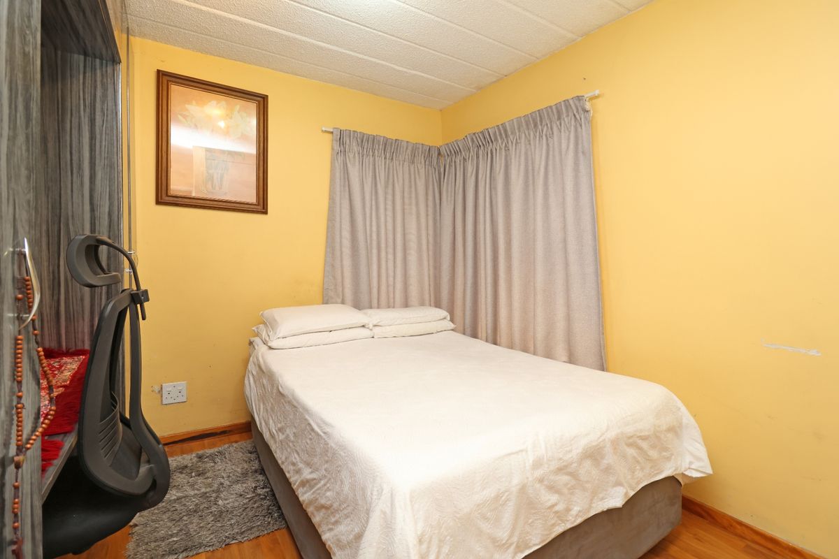 A compact bedroom featuring laminate flooring and yellow painted walls, currently furnished with a bed and window curtains.