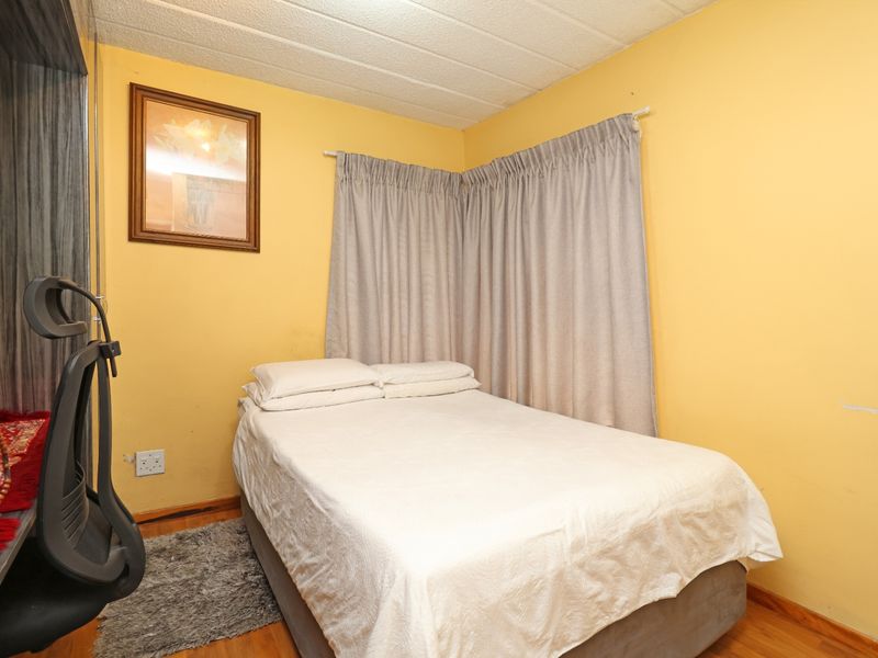 A compact bedroom featuring laminate flooring and yellow painted walls, currently furnished with a bed and window curtains.