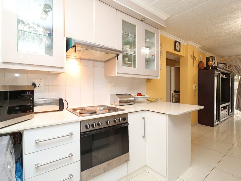 Open-plan kitchen featuring white cabinetry, stone countertops, integrated oven and stove, and tiled flooring, seamlessly flowing into the adjacent living area.