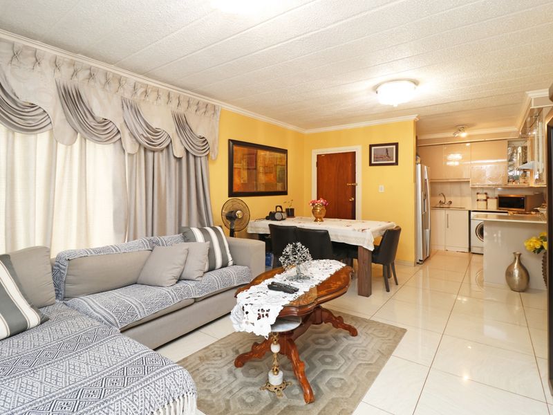 Open-plan living and dining area featuring tiled flooring and a compact, modern kitchen with glossy cabinetry and integrated appliances.
