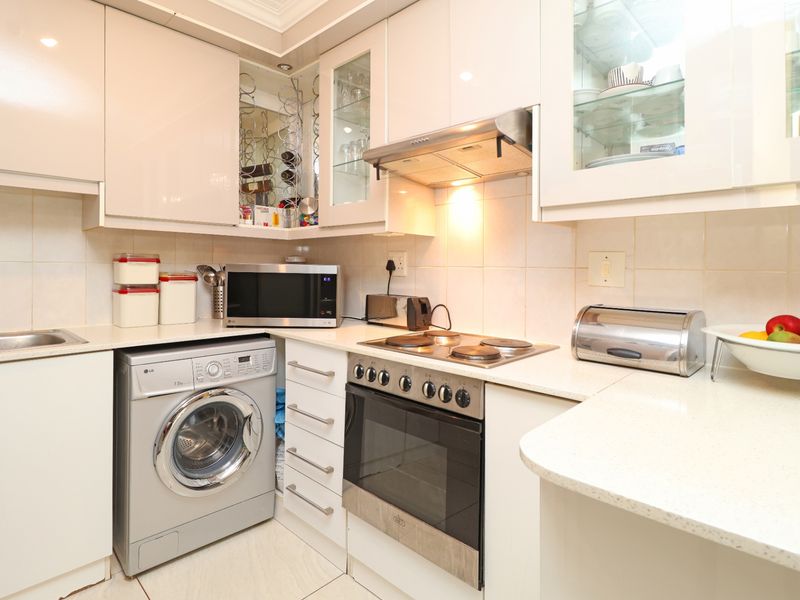 Compact, well-maintained kitchen featuring white high-gloss cabinetry, stone countertops, integrated appliances, and a tiled backsplash.