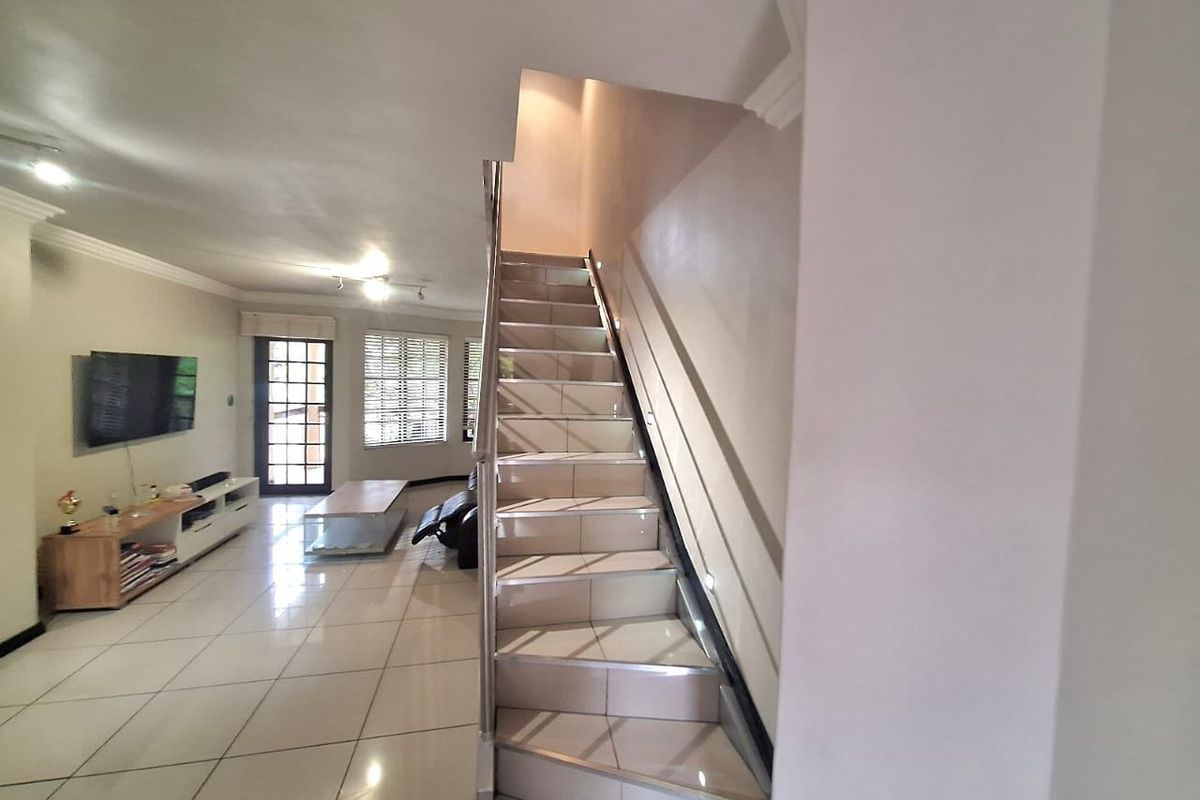 Open plan living area featuring tiled flooring, a central staircase with a metal handrail, and access to an outdoor area via a french door.