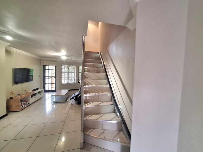 Open plan living area featuring tiled flooring, a central staircase with a metal handrail, and access to an outdoor area via a french door.