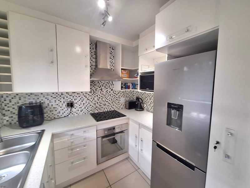 A functional kitchen featuring white cabinetry, stone countertops, a mosaic tile backsplash, and integrated stainless steel appliances including an oven and extractor fan.