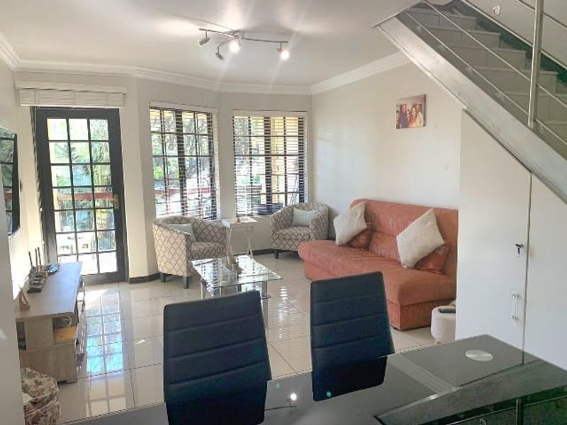 Open-plan living area featuring tiled floors, a staircase with metal balustrades, and large windows providing natural light and access to the exterior.