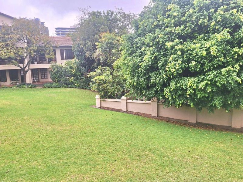 A well-maintained communal garden area featuring a large lawn, mature trees, and a perimeter wall, providing a pleasant outdoor space for residents.