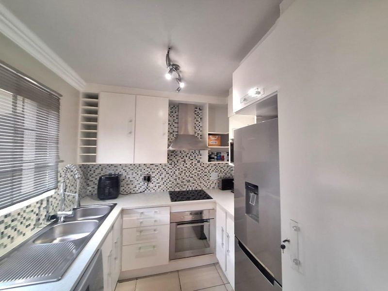 A functional kitchen featuring white cabinetry, mosaic tile backsplash, stainless steel appliances, and a double sink with a modern mixer tap.