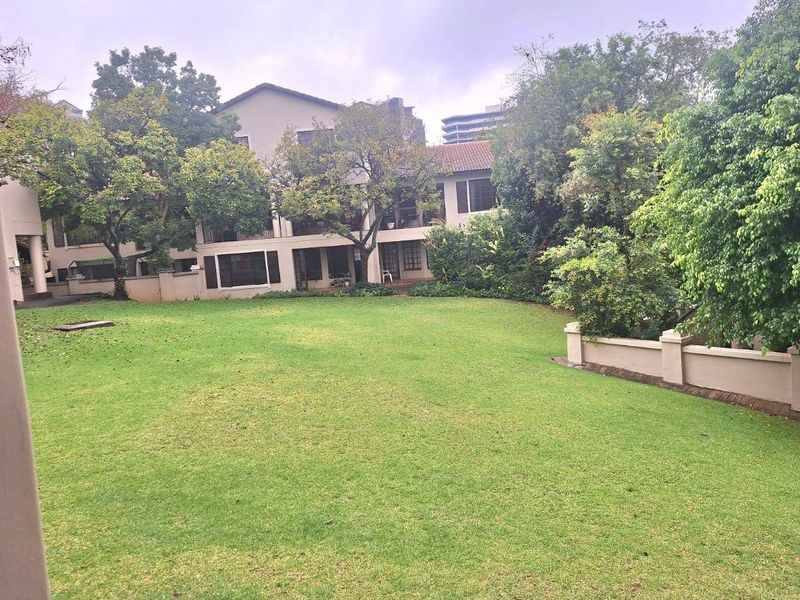 A view of the rear exterior of the apartment complex, featuring a large, well-maintained lawn and mature trees.